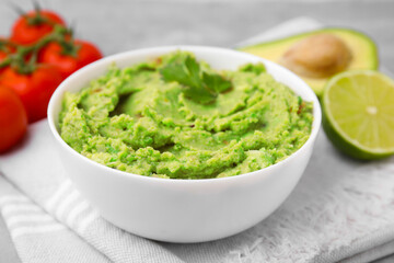 Bowl of delicious guacamole and ingredients on cloth, closeup