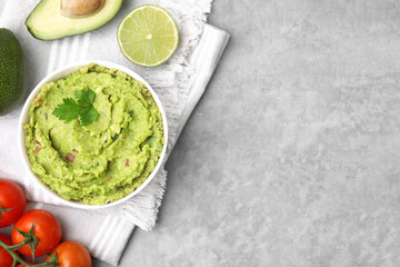 Bowl of delicious guacamole and ingredients on grey table, flat lay. Space for text