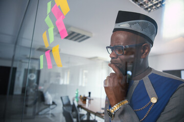 An African businessman looks thoughtfully at the sticky notes hanging on the wall