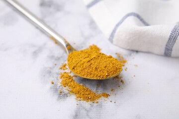 Spoon with curry powder on white marble table, closeup