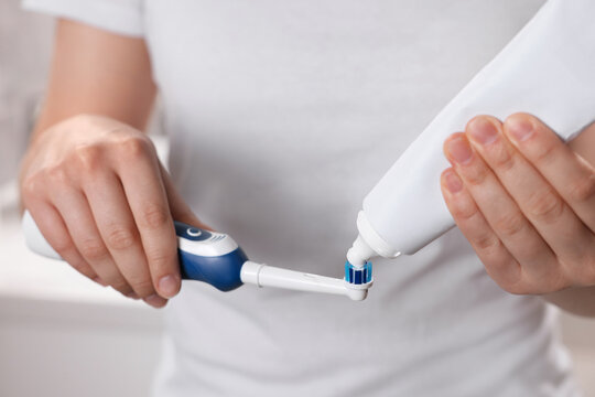 Woman squeezing toothpaste from tube onto electric toothbrush, closeup