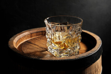 Glass of whiskey on wooden barrel against black background, closeup