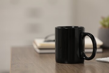 Black ceramic mug and notebooks on wooden table at workplace. Space for text