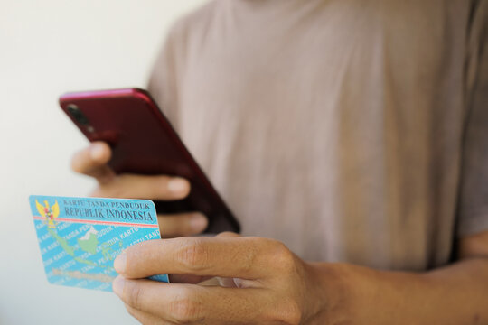 Asian man takes a photo of his Indonesian National Identity Card (KTP) using a mobile phone