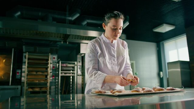 beautiful woman baker tears ready freshly baked hot aromatic buns and checks dough bakery production