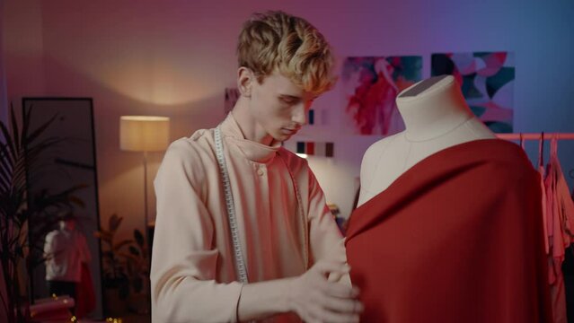 Male tailor putting red textile on mannequin while creating new garment in his fashion design studio