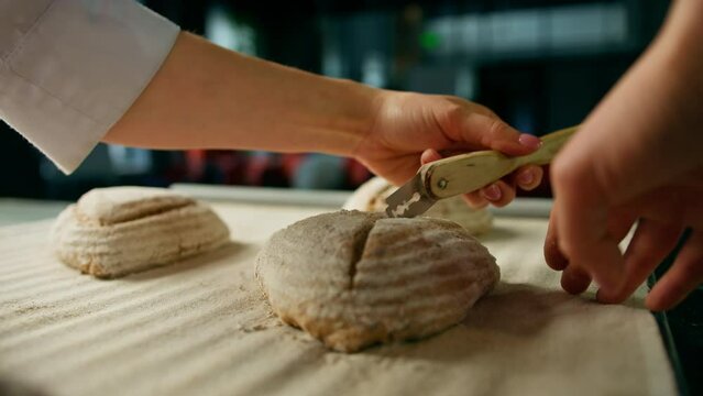woman baker cuts patterns on raw bread rolls with a professional baker's knife before baking bakery production of pastries close-up