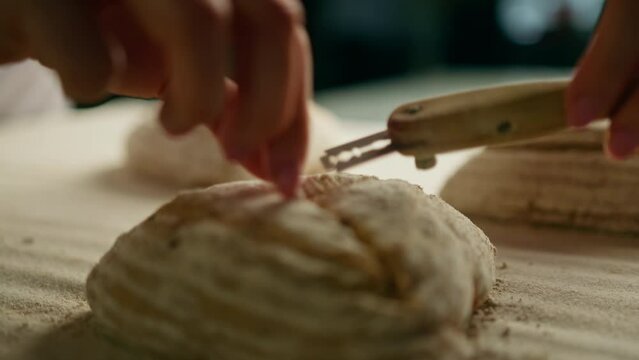 woman baker cuts patterns on raw bread rolls with a professional baker's knife before baking bakery production of pastries close-up