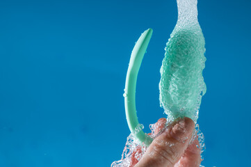 A woman washes a vibrator under running water on a blue background. Women's Health Kegel Trainer. 