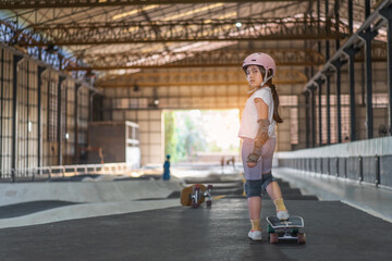asian child skater or kid girl fun playing skateboard or start ride surf skate at indoor pump track skate park by extreme sports surfing to wears helmet elbow pads wrist knee guard for body safety