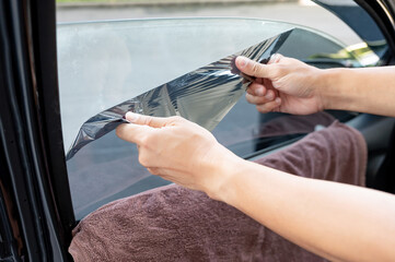 Car side window film removal and tinting installation. Male auto specialist worker hand gently carefully peeling off the old protective car film from glass surface. - 609532161