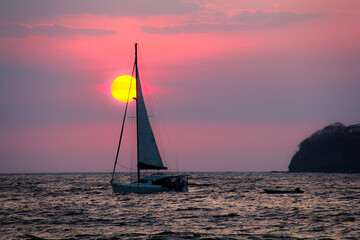 Obraz na płótnie Canvas A lone sailboat against a sunset in the pacific ocean off the coast of Costa Rica.
