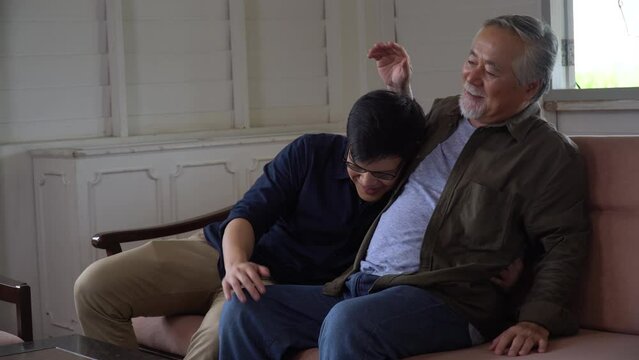 asian senior father embracing comforting pat back talking and laughing wirh adult  son on sofa in living room at home. happy family love .