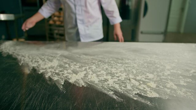 professional chef throws flour on table making flour clouds before preparing bread pastry in bakery in professional kitchen