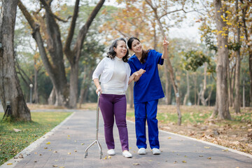 Obraz premium Patient care, female care, young Asian women are taking care of the elderly, providing crutches and walking for patients, and exercising their legs and knees in the park parks.