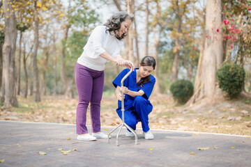 Patient care, female care, young Asian women are taking care of the elderly, providing crutches and walking for patients, and exercising their legs and knees in the park parks.