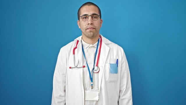 Young hispanic man saying no with finger over isolated blue background