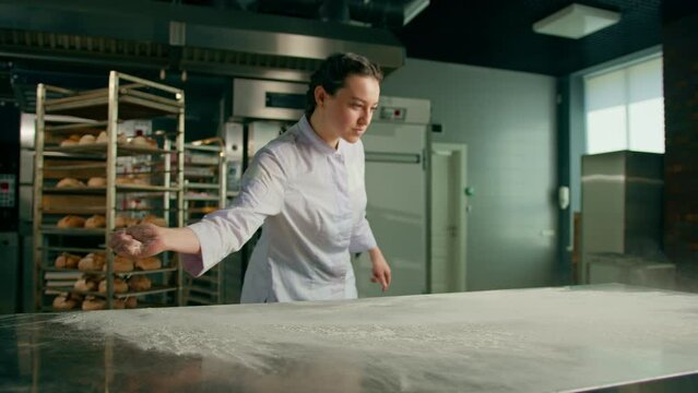 professional chef throws flour on table making flour clouds before preparing bread pastry in bakery in professional kitchen