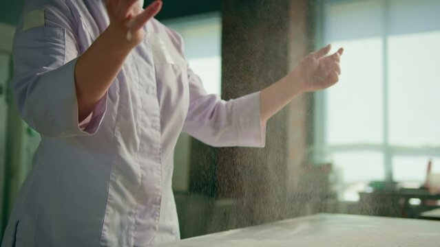 professional chef throws flour on table making flour clouds before preparing bread pastry in bakery in professional kitchen