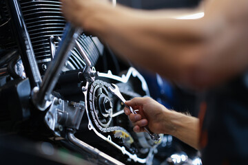 Male mechanic repairs amotorcycle motor with wrench in service center. Motorcycle maintenance and...