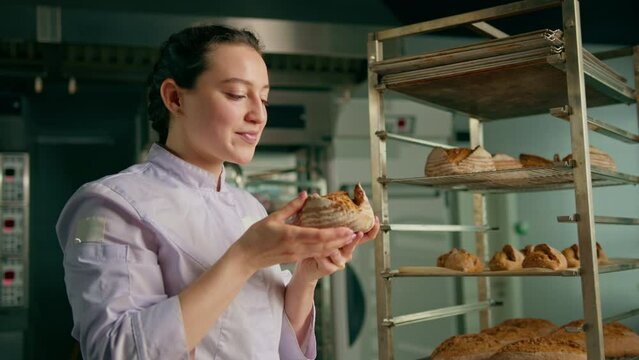 attractive female baker takes freshly baked fragrant bread from the shelf sniffs it checks its quality bakery professional kitchen baking