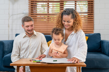 Enjoy happy smiling love family father and mother with little girl learning and writing in book with pencil making homework at home. Education concept