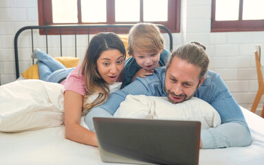 Happy family people leisure in bedroom together. Father and mother with son relaxing and using laptop on bed