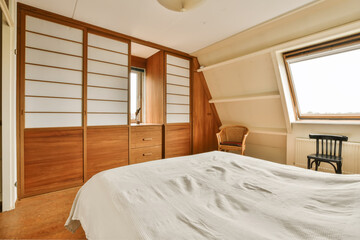 a bedroom with a bed, dresser and window in the corner to the left is an empty chair on the right side