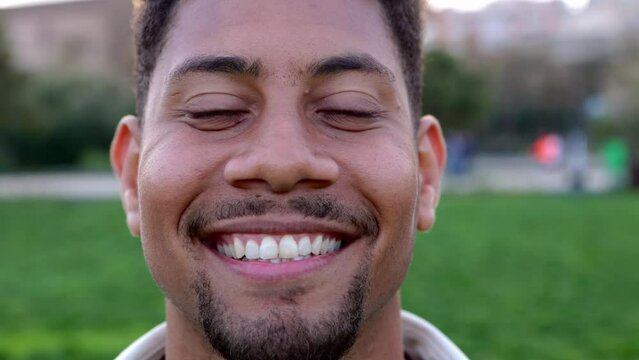 Close up portrait of happy african american young man standing in city park. Successful male model face smiling at camera outdoors. Positive people and youth concept.