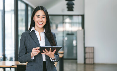 Young attractive businesswoman holding tablet, smiling to camera, standing in office.