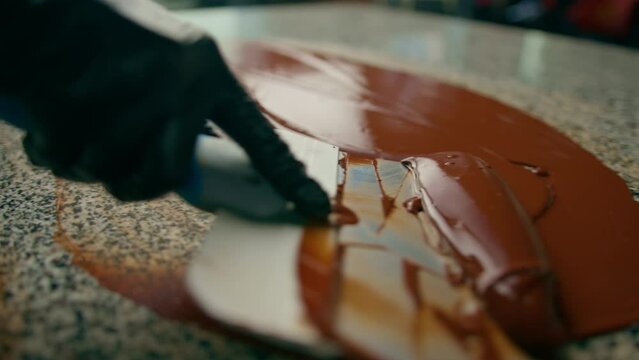 Tempering chocolate production of chocolate candies - pastry chef mixes melted chocolate with a metal spatula on a table in a pastry shop