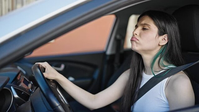 Young beautiful hispanic woman stressed sitting on car at street