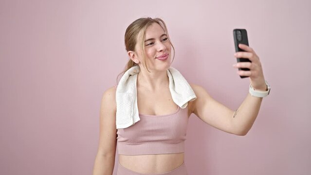 Young blonde woman make selfie by smartphone doing strong gesture with arm over isolated pink background