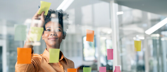 Happy black businesswoman planning new porject with sticky note in a creative office