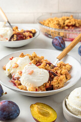 Fruit crumble. Plum crumble pie with vanilla ice cream in plates with spoons on white marble table for tasty breakfast