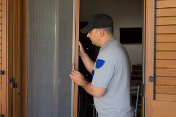 Image of a handyman installing a fly screen in a French window of his house. Protection of the house from insects.
