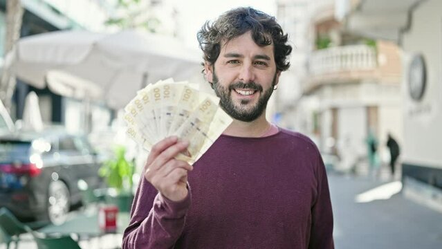 Young hispanic man smiling confident holding denmark krone banknotes at coffee shop terrace