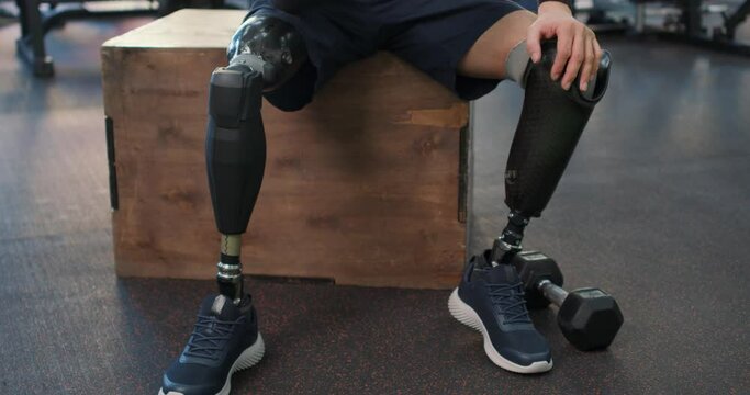young serious motivated disabled man doing dumbbell workout at gym working on arms strength, looking at his biceps, copy space. Athletic man lifting dumbells up weightlifting lifestyle workout routine