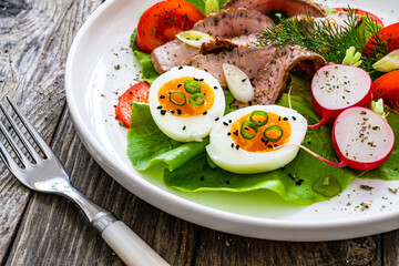 Tasty salad - roasted beef loin boiled eggs and fresh vegetables on wooden table
