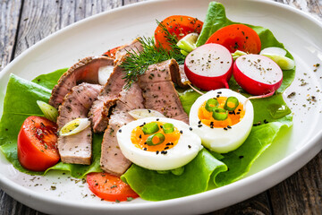 Tasty salad - roasted beef loin boiled eggs and fresh vegetables on wooden table
