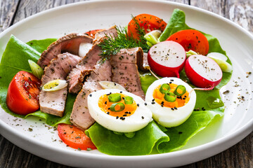 Tasty salad - roasted beef loin boiled eggs and fresh vegetables on wooden table
