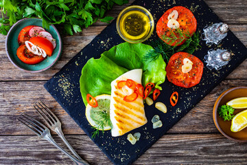 Grilled calamari steak with fried tomatoes and fresh vegetables on wooden table
