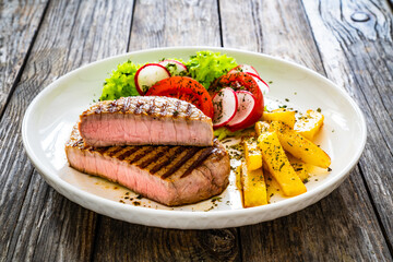 Grilled beef steaks with fresh vegetable salad and French fries on wooden table
