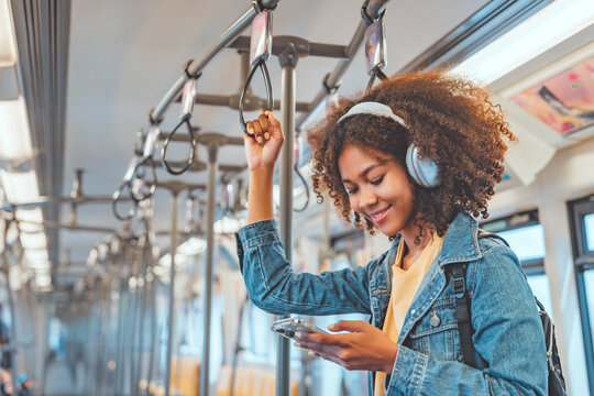 Happy young African American woman passenger listening music via smart mobile phone in a train, Smile female wearing wireless headphones while moving in the tram, lifestyle, transportation