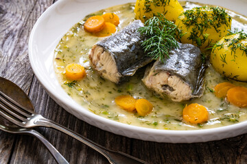 Cooked eel steaks and boiled tomatoes in dill sauce served on wooden table
