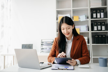 Confident Asian woman with a smile standing holding notepad and tablet at the modern office..