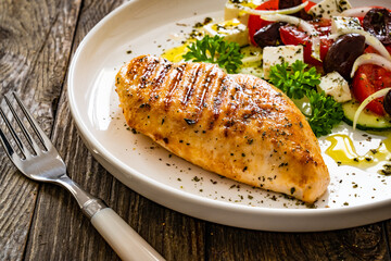 Seared chicken breast and Greek salad on wooden table
