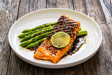 Grilled salmon steak with green asparagus in teriyaki sauce on wooden table
