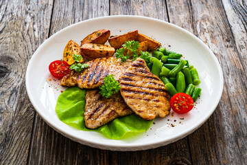 Grilled pork loin steaks with green beans and fried potatoes on wooden table
