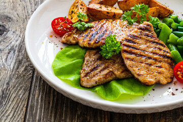 Grilled pork loin steaks with green beans and fried potatoes on wooden table
